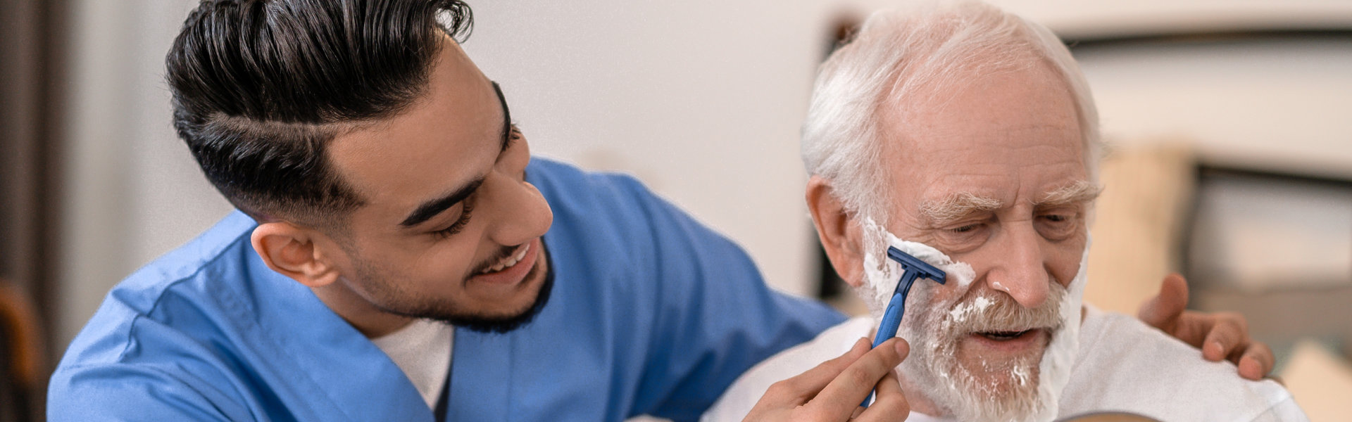 caregiver shaving the elderly man's beard